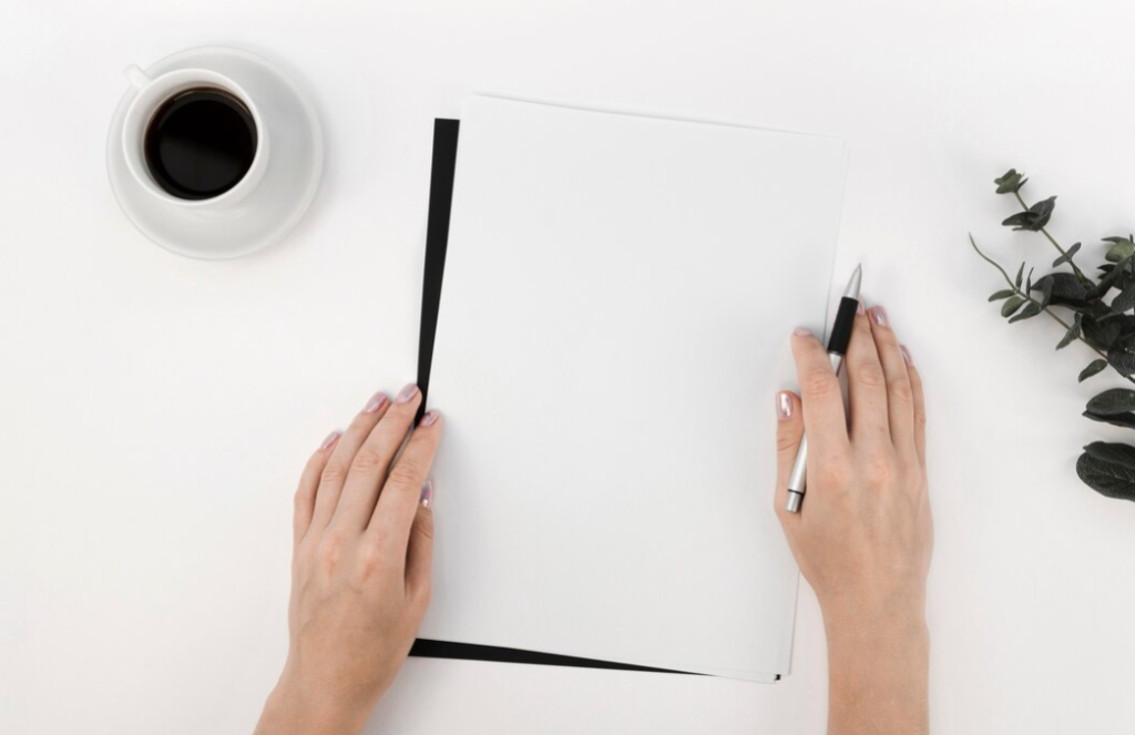 hands with pen on the white sheet, a cup of coffee, and green  flower  on the white table