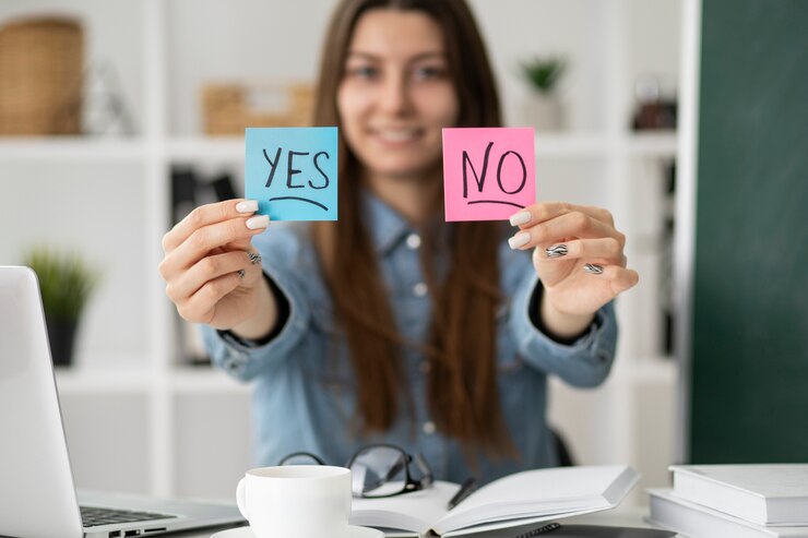 a young woman sitting, smiling, and holding sticky notes labeled “YES” and “NO